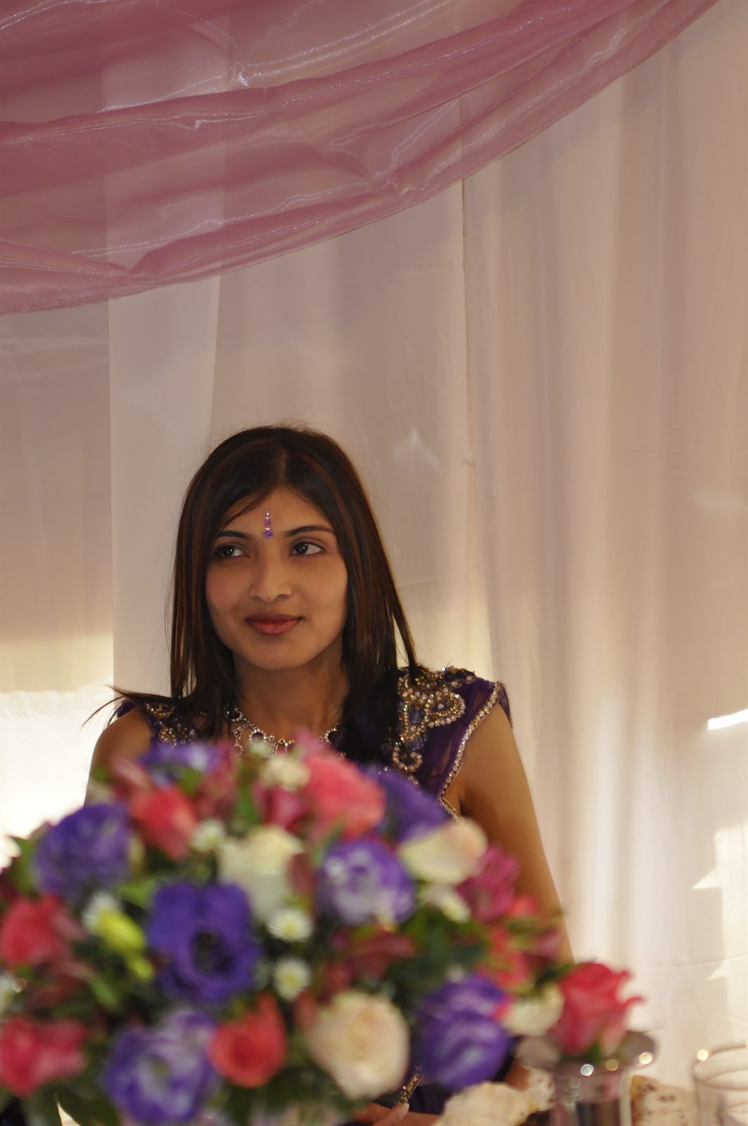 A bride seated behind wedding flowers, photographed candidly