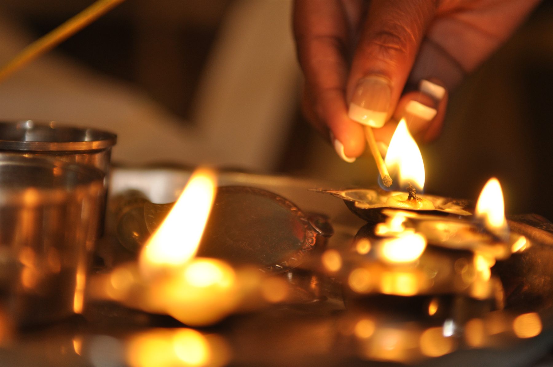 A hand lighting rows of small oil lamps at dusk