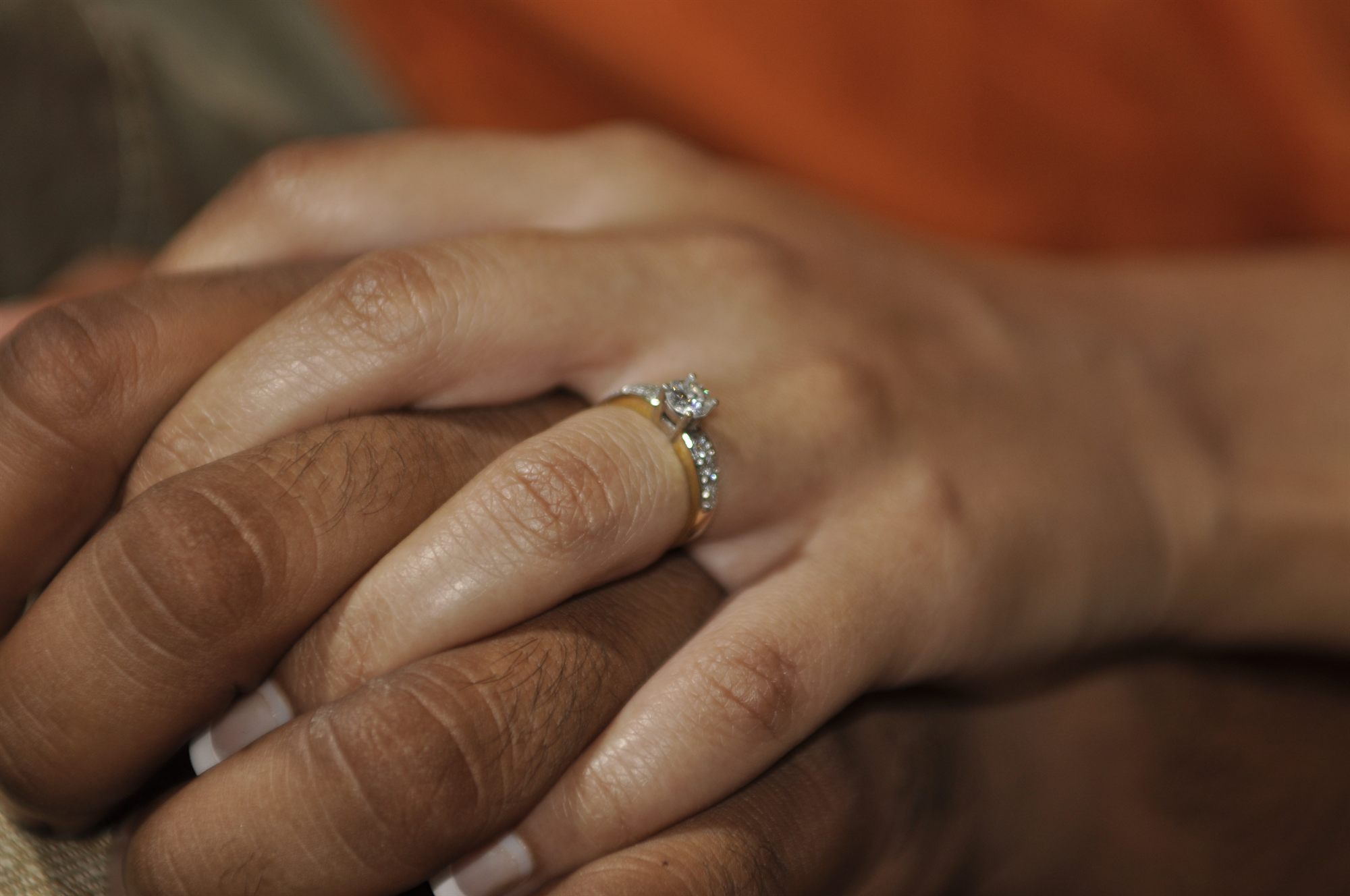 Two hands clasped, an engagement ring catching the light